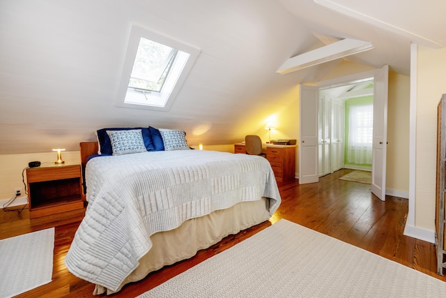 bedroom featuring lofted ceiling with skylight, baseboards, and hardwood / wood-style floors