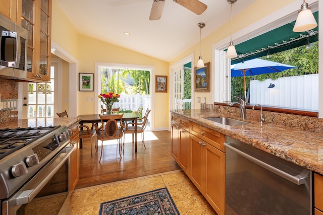 kitchen featuring pendant lighting, stainless steel appliances, lofted ceiling, a sink, and light stone countertops