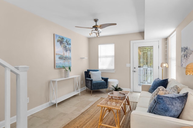 living area with stone tile floors, baseboards, and a ceiling fan