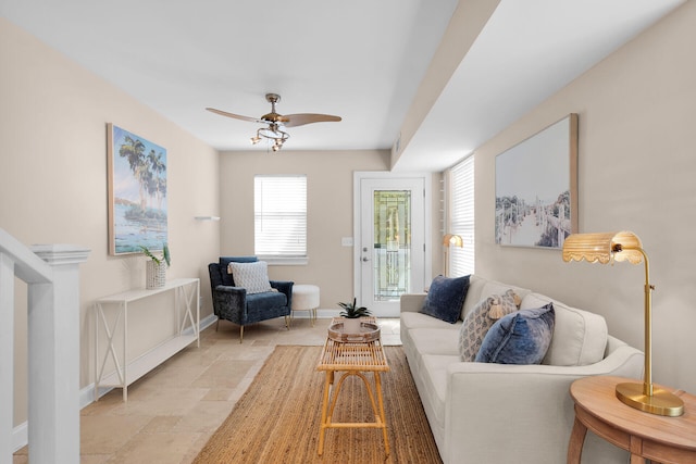 living area featuring baseboards, a ceiling fan, and stone tile flooring