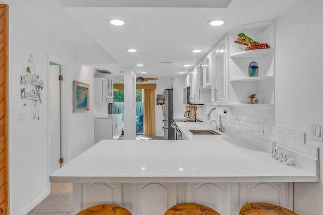 kitchen with stainless steel refrigerator, white cabinetry, kitchen peninsula, and sink