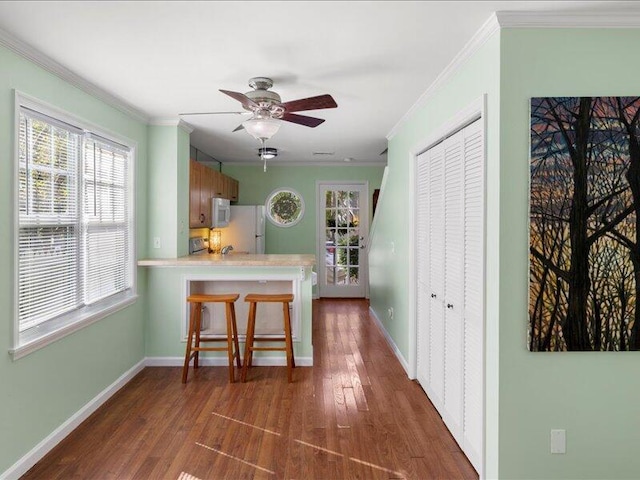 kitchen featuring dark hardwood / wood-style flooring, ornamental molding, ceiling fan, kitchen peninsula, and white appliances