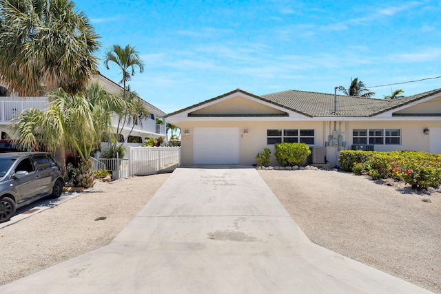 ranch-style home featuring a tile roof, driveway, fence, a garage, and stucco siding