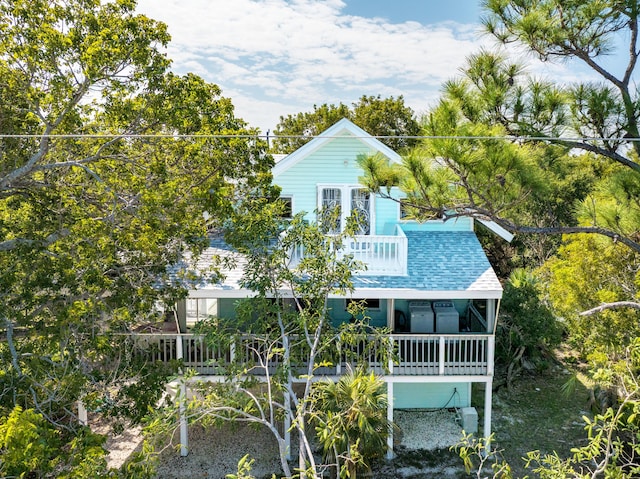 rear view of house featuring a shingled roof and a balcony