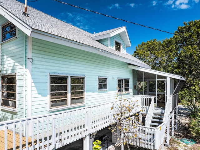 view of side of property featuring a deck, stairs, roof with shingles, and a sunroom