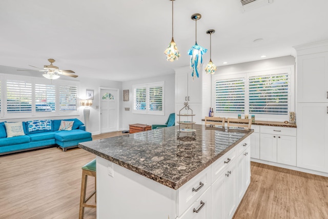 kitchen with visible vents, a kitchen island, a breakfast bar area, light wood-style floors, and white cabinetry