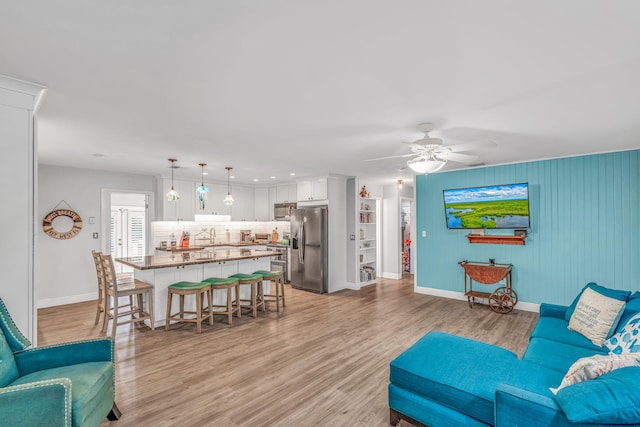 living room featuring a ceiling fan, baseboards, and light wood finished floors