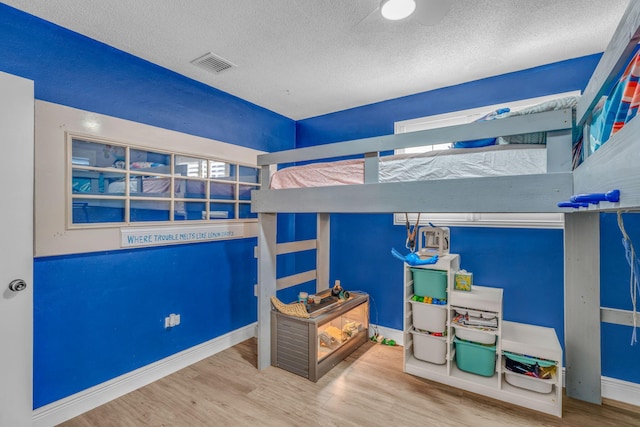 bedroom featuring baseboards, a textured ceiling, visible vents, and wood finished floors