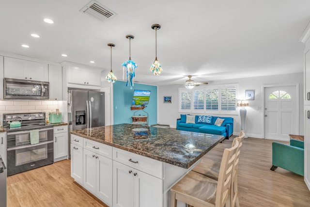 kitchen with stainless steel appliances, visible vents, light wood-style floors, open floor plan, and decorative backsplash