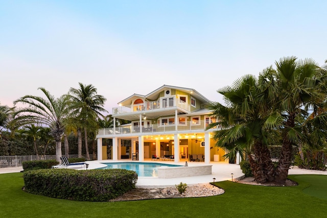 back house at dusk with a balcony, a lawn, and a patio area