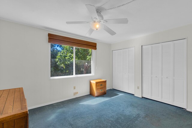 unfurnished bedroom featuring multiple closets, dark colored carpet, and ceiling fan