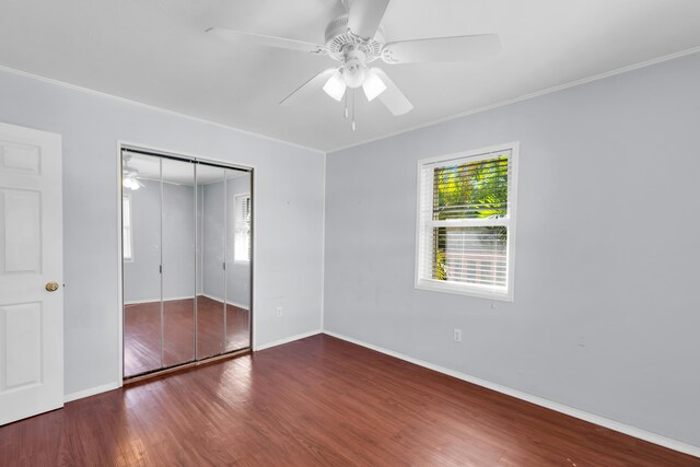 unfurnished bedroom with crown molding, dark wood-type flooring, a closet, and ceiling fan