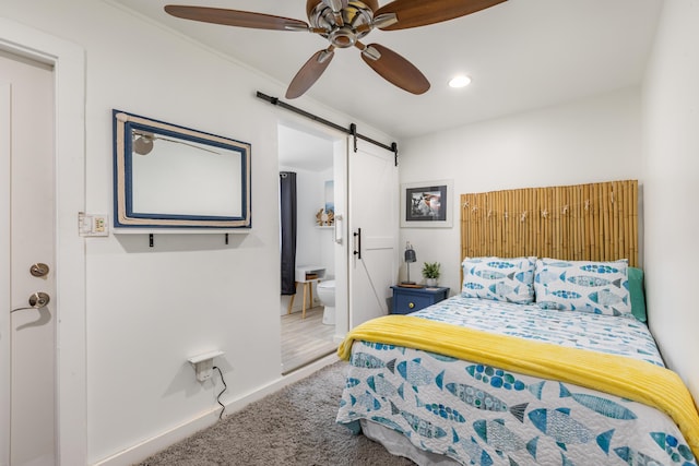 carpeted bedroom with a barn door, connected bathroom, and ceiling fan