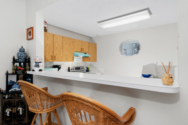 kitchen featuring a breakfast bar, light countertops, a textured ceiling, stainless steel range with electric cooktop, and under cabinet range hood