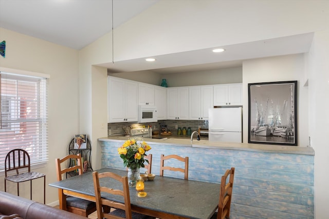 kitchen with lofted ceiling, light countertops, decorative backsplash, white cabinets, and white appliances