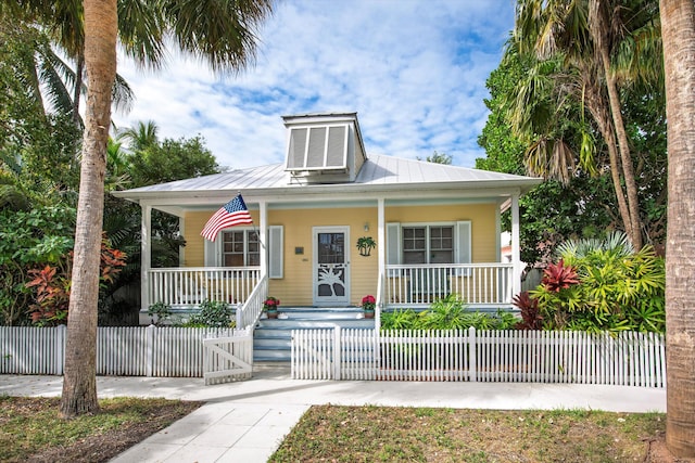 bungalow-style home with metal roof, a porch, and a fenced front yard