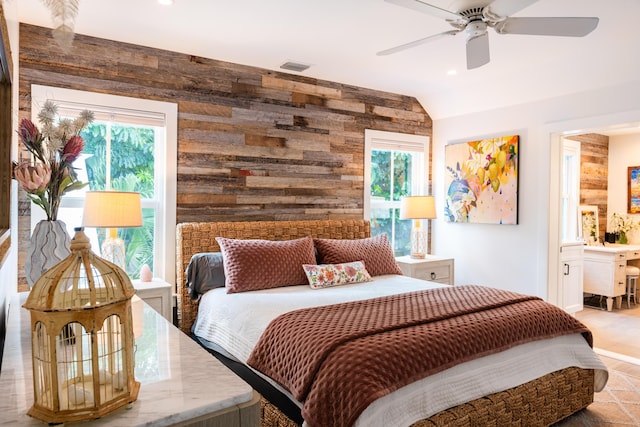 bedroom with ceiling fan, ensuite bathroom, vaulted ceiling, and wood walls