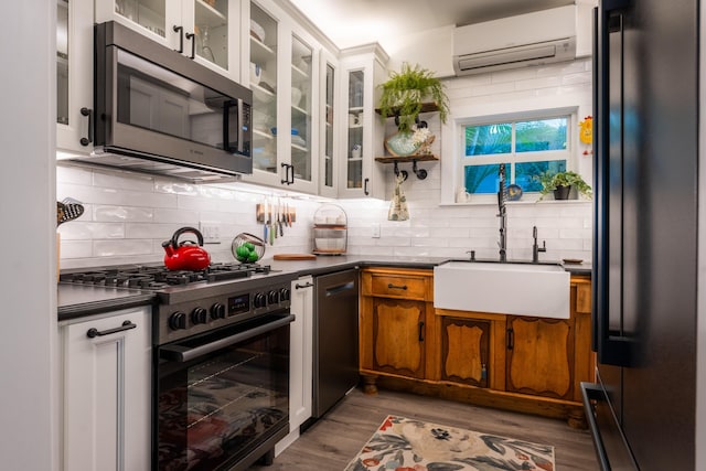 kitchen with sink, light hardwood / wood-style flooring, appliances with stainless steel finishes, a wall mounted AC, and tasteful backsplash