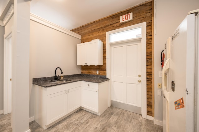 kitchen featuring white cabinetry, sink, wooden walls, and light wood-type flooring