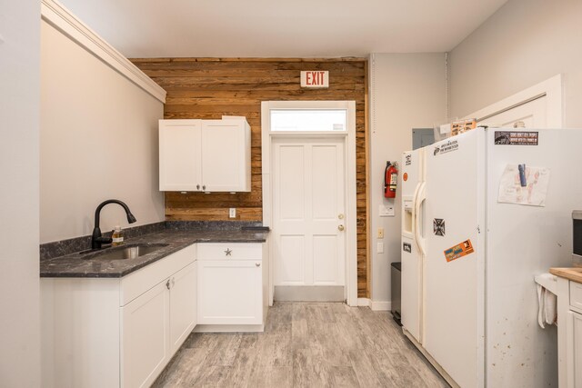 kitchen with wooden walls, white cabinetry, sink, white fridge with ice dispenser, and light hardwood / wood-style flooring