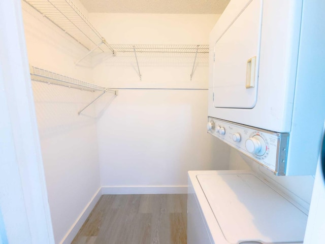 spacious closet featuring stacked washer and dryer and light wood-type flooring