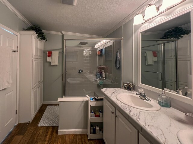 full bath with a textured ceiling, wood finished floors, vanity, ornamental molding, and a shower stall