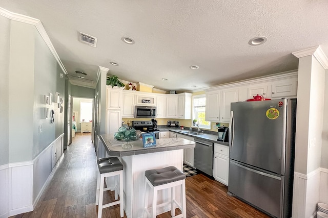 kitchen with stainless steel appliances, dark countertops, a center island, and white cabinetry