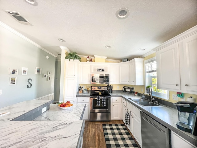 kitchen featuring a sink, visible vents, white cabinets, appliances with stainless steel finishes, and crown molding