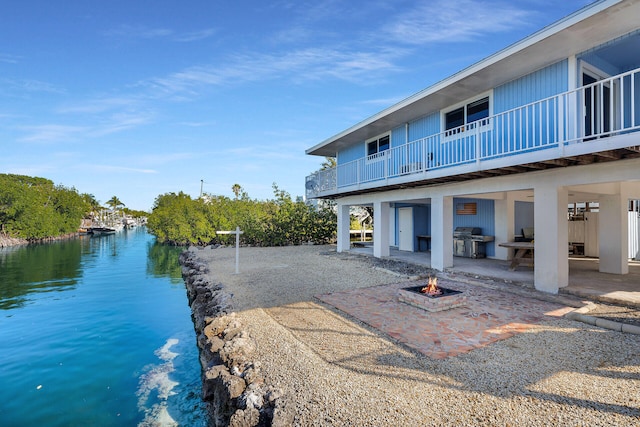 back of house with a water view, an outdoor fire pit, and a patio