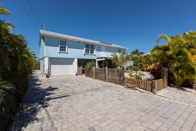 coastal inspired home with decorative driveway, a garage, and a fenced front yard