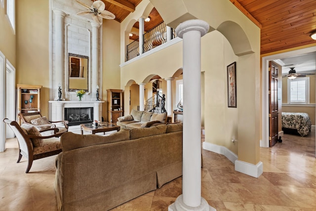 living room with wood ceiling, ceiling fan, decorative columns, a high ceiling, and a fireplace