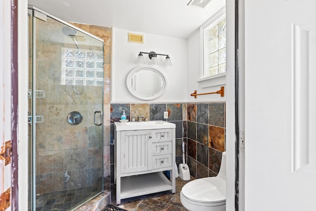 bathroom featuring a shower with door, vanity, tile walls, and toilet