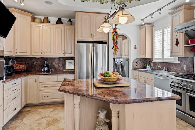 kitchen with decorative light fixtures, a center island, separate washer and dryer, appliances with stainless steel finishes, and wall chimney range hood