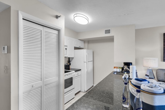 kitchen featuring light tile patterned flooring, white cabinetry, a textured ceiling, dark stone countertops, and white appliances