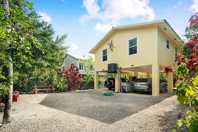 back of house featuring a carport, gravel driveway, central AC, and stucco siding