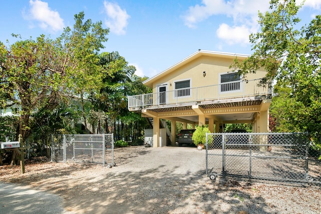 view of front facade with a carport, a gate, dirt driveway, fence, and stucco siding
