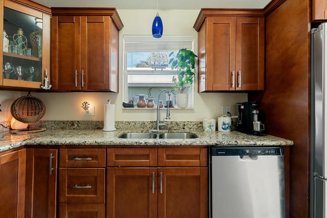kitchen with appliances with stainless steel finishes, a sink, light stone counters, glass insert cabinets, and pendant lighting