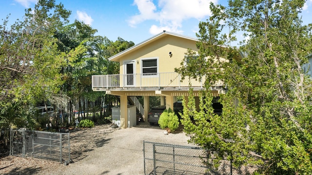 view of front of home with a carport, driveway, stucco siding, a deck, and fence