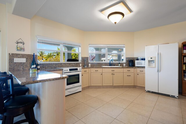 kitchen featuring white appliances, kitchen peninsula, backsplash, sink, and dark stone countertops