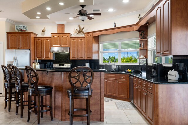 kitchen featuring tasteful backsplash, stainless steel appliances, crown molding, a kitchen island, and a kitchen bar