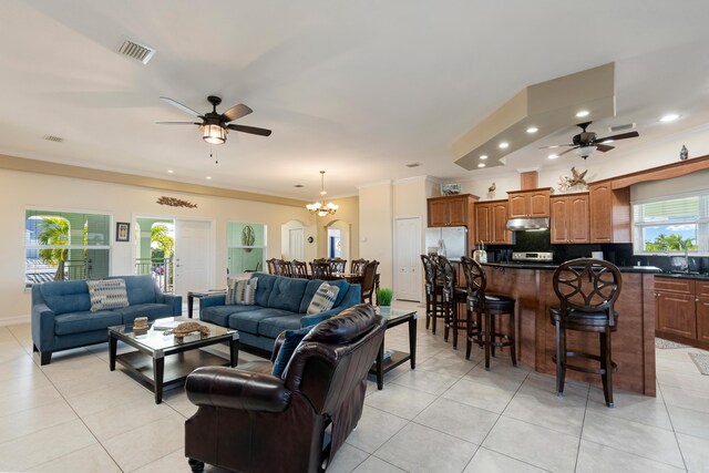 tiled living room featuring ceiling fan with notable chandelier, crown molding, and sink