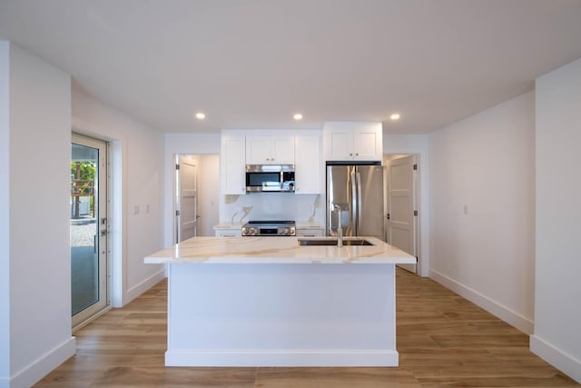 kitchen featuring appliances with stainless steel finishes, an island with sink, white cabinets, light stone counters, and light hardwood / wood-style floors