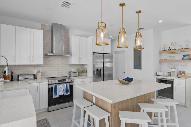 kitchen featuring pendant lighting, wall chimney range hood, appliances with stainless steel finishes, white cabinetry, and a kitchen island