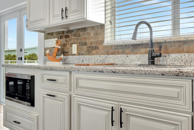 kitchen featuring sink, backsplash, a wealth of natural light, and light stone countertops