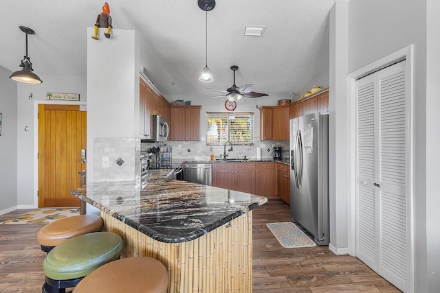 kitchen with pendant lighting, a breakfast bar, appliances with stainless steel finishes, backsplash, and kitchen peninsula