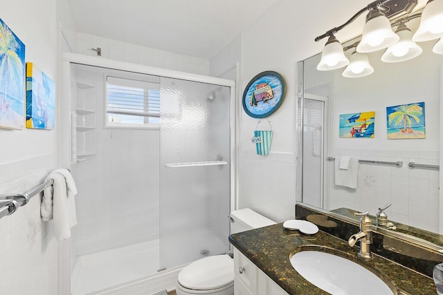 bathroom featuring a shower with door, vanity, tile walls, and toilet