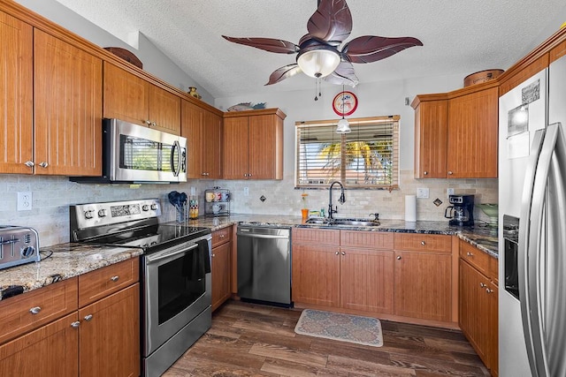 kitchen with sink, a textured ceiling, appliances with stainless steel finishes, dark hardwood / wood-style floors, and dark stone counters