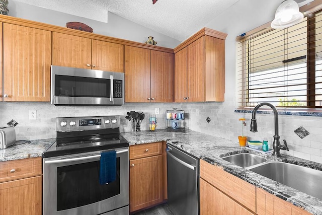 kitchen with sink, appliances with stainless steel finishes, light stone counters, a textured ceiling, and vaulted ceiling