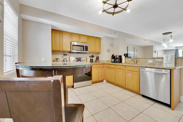 kitchen featuring hanging light fixtures, light tile patterned floors, appliances with stainless steel finishes, kitchen peninsula, and light stone countertops