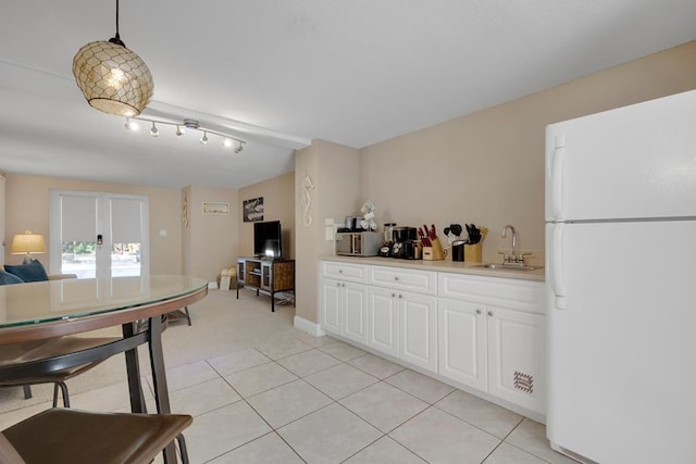 kitchen with decorative light fixtures, white cabinetry, sink, white fridge, and light tile patterned floors